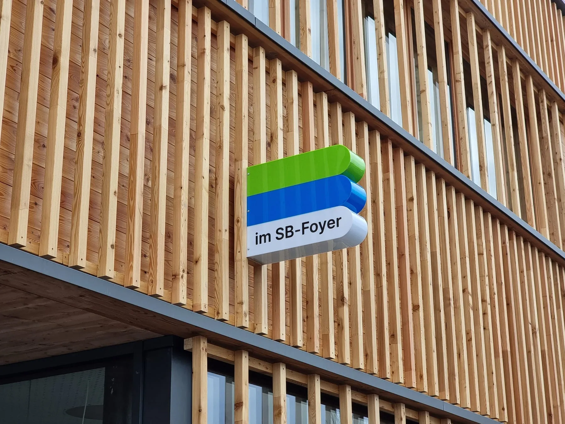 Zusatzschild „im SB-Foyer“ an der Lattenfassade einer Sparkasse-Filiale