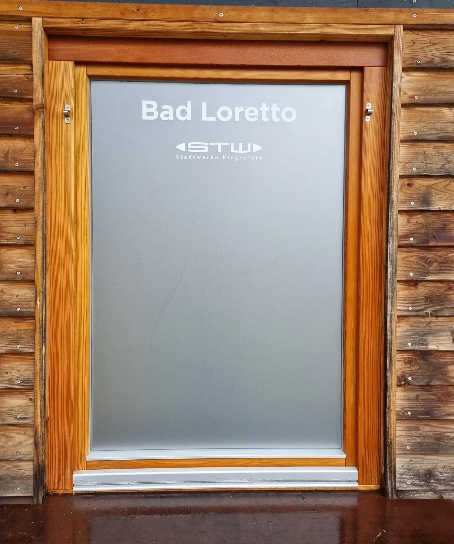 Holztür im Bad Loretto mit Milchglasfolie, Schriftzug und Logo der Stadtwerke Klagenfurt