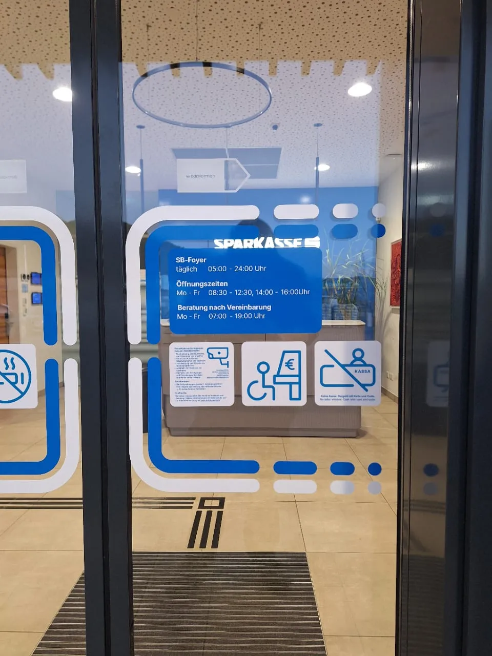 Glastür zum SB-Foyer einer Sparkasse mit Dekorfolie, Öffnungszeiten und Piktogrammen