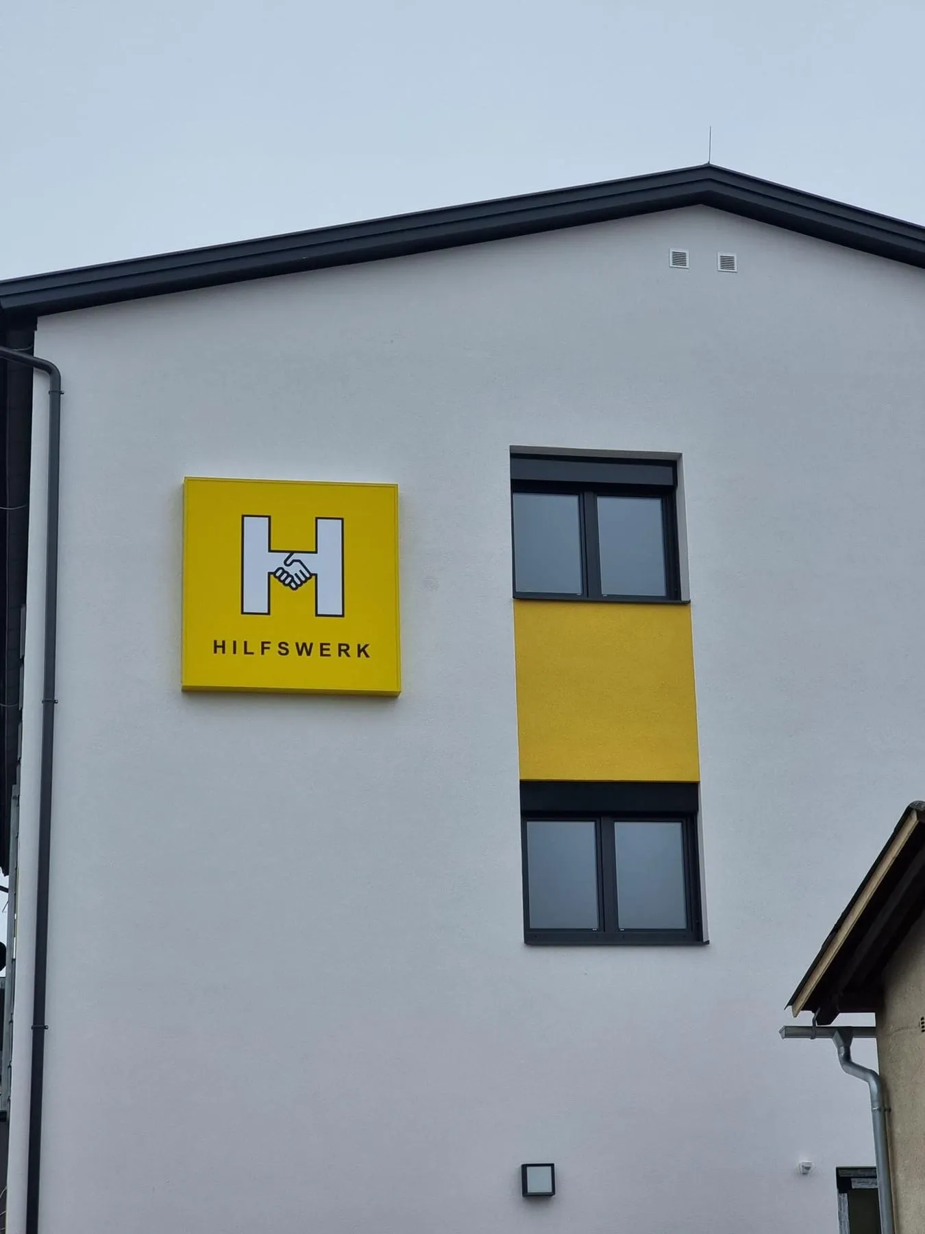 Fertiges gelbes Hilfswerk-Leuchtschild an der weißen Westfassade