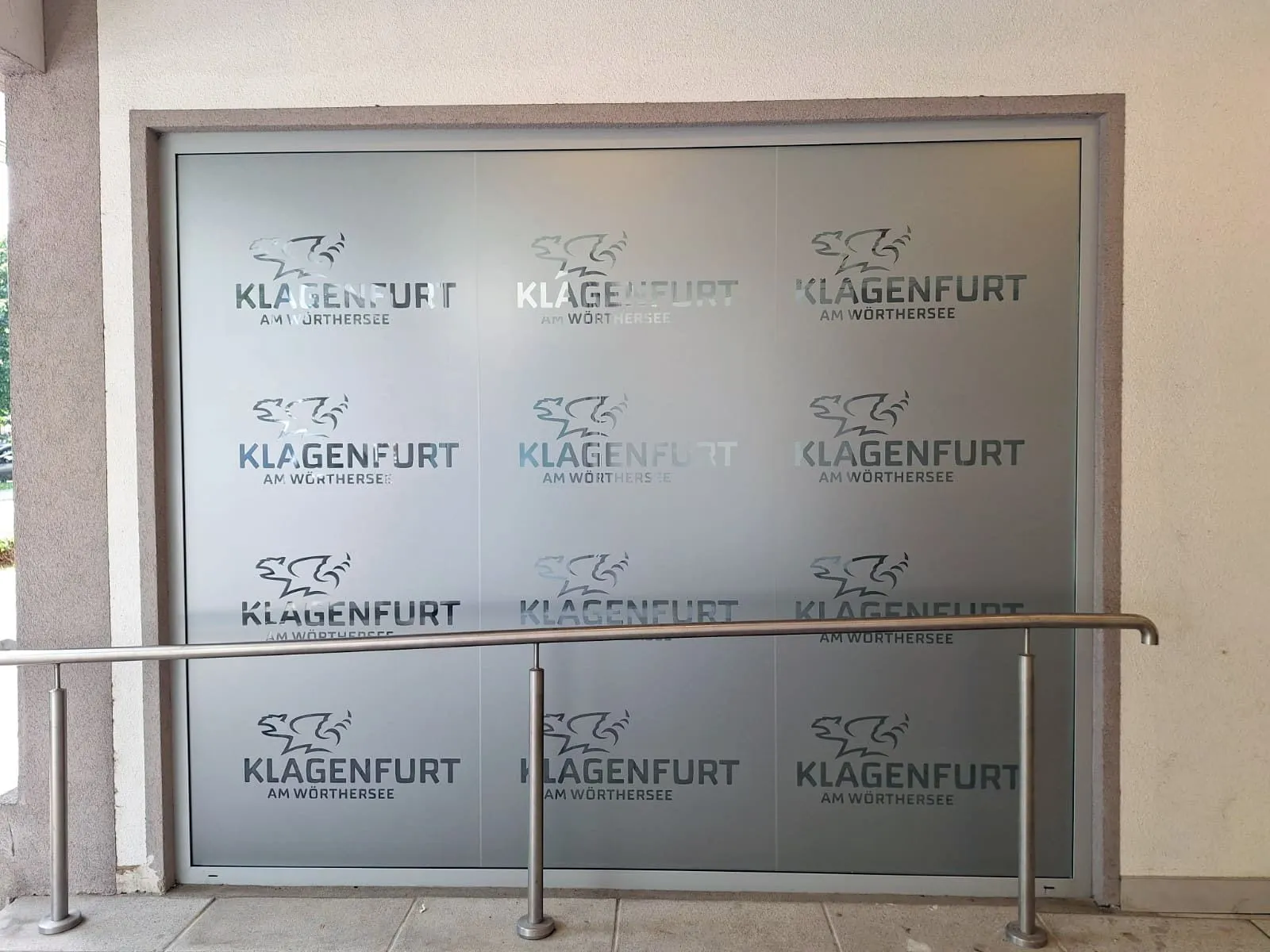 Milchglasfolie geschnitten: Stadtlogo „Klagenfurt am Wörthersee“ als Rapport über eine große Glasfläche