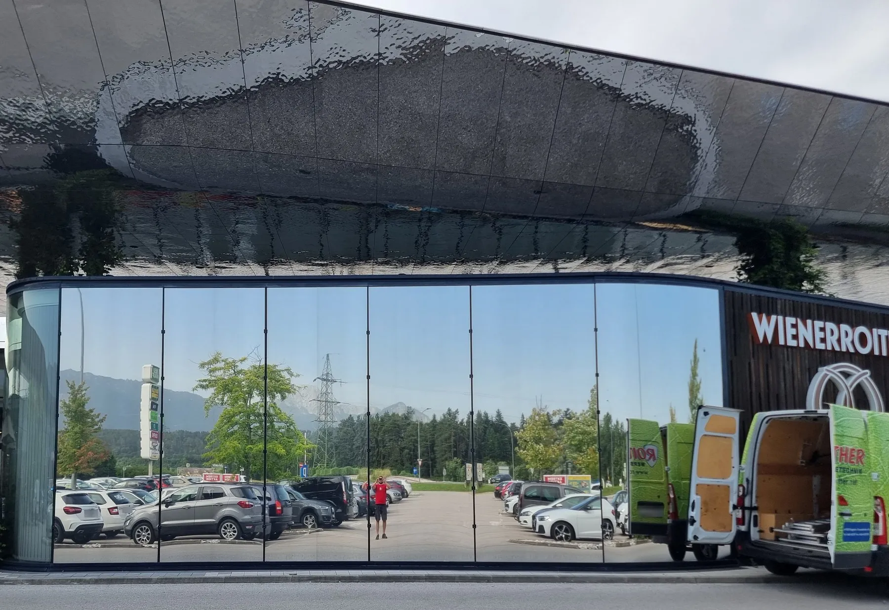 Runder Glaspavillon mit Sonnenschutzfolie, die Scheiben spiegeln Parkplatz und Himmel
