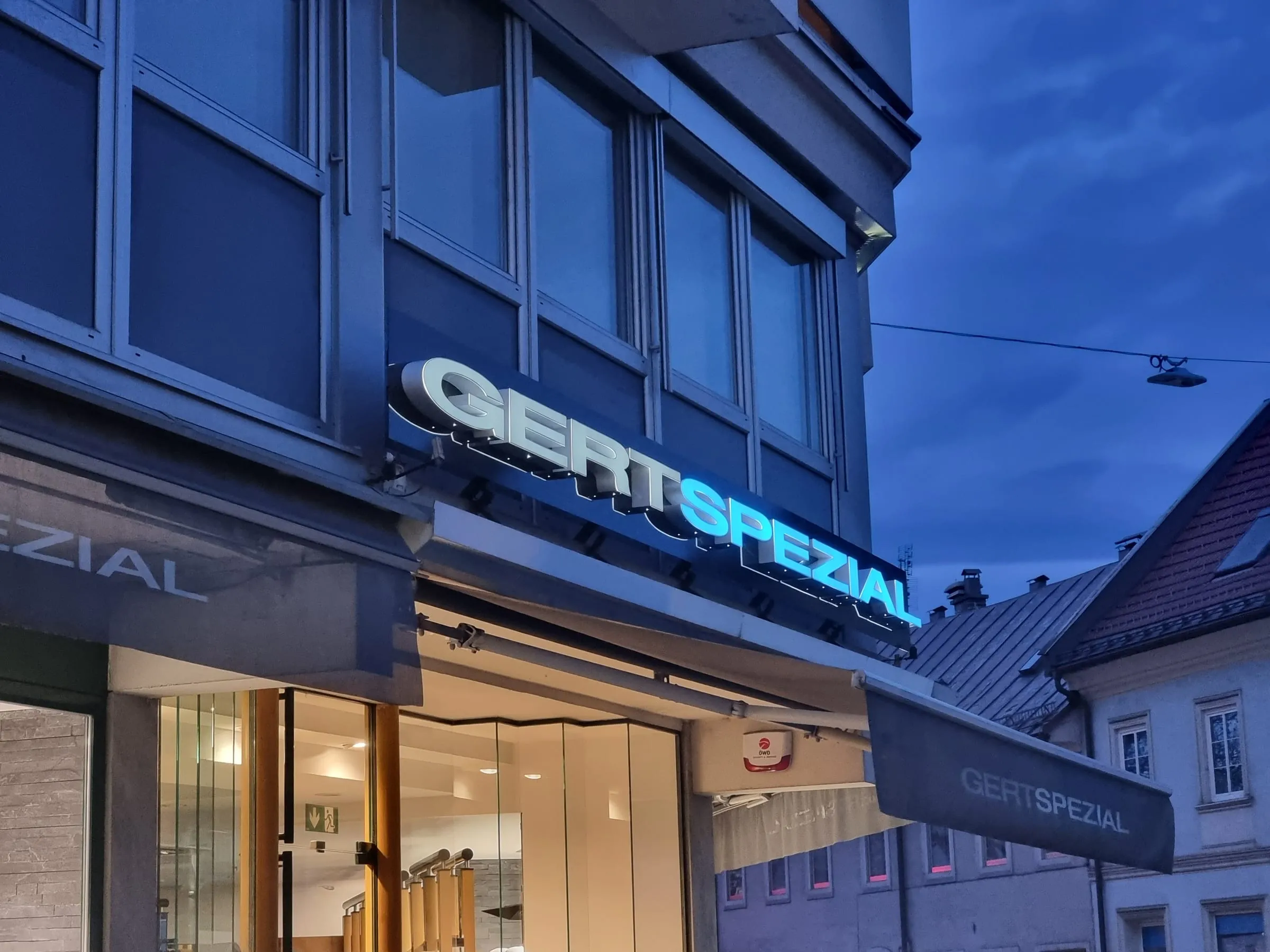 Leuchtbuchstaben GERTSPEZIAL in der blauen Stunde: SPEZIAL leuchtet blau über dem hell beleuchteten Geschäft
