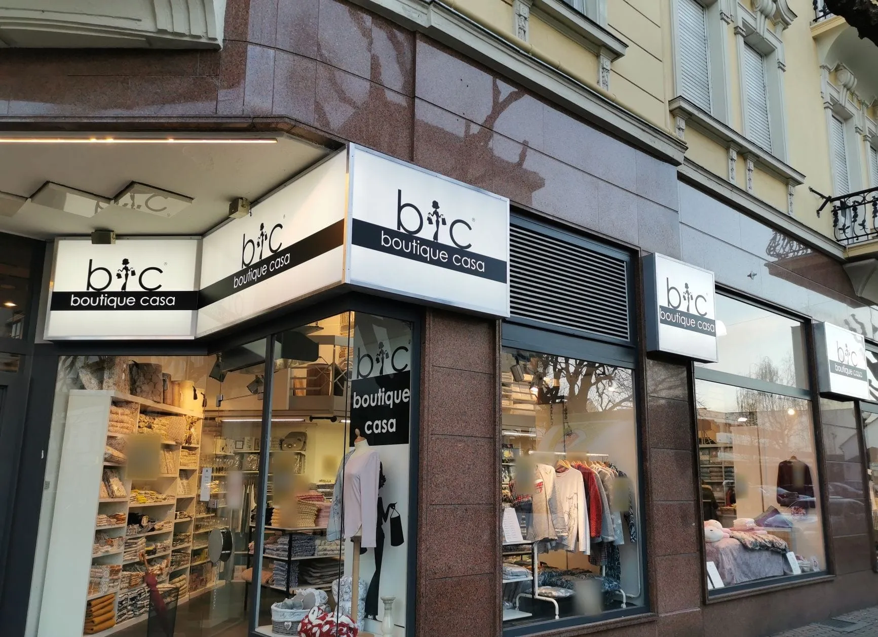 Flache Leuchtkästen über den Schaufenstern einer Eckfassade, in der Dämmerung