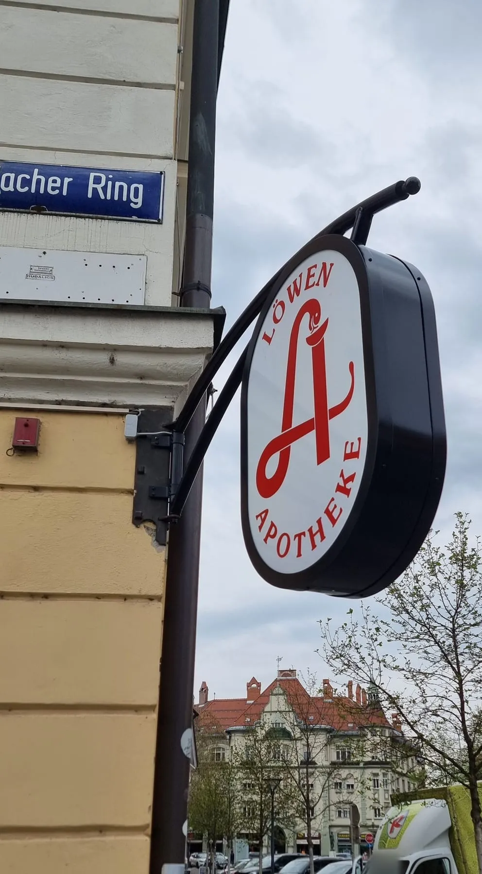 Ausleger an einem geschwungenen Wandarm, quer zur Hausfassade über dem Gehsteig