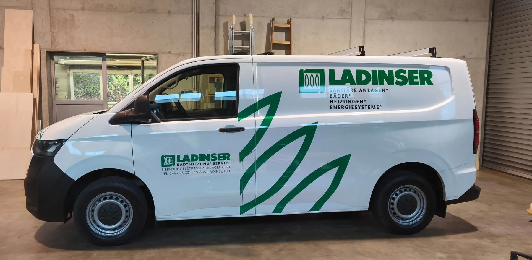Weißer Transporter mit grüner Blattgrafik und Firmenschriftzug, Seitenansicht in unserer Werkstatt