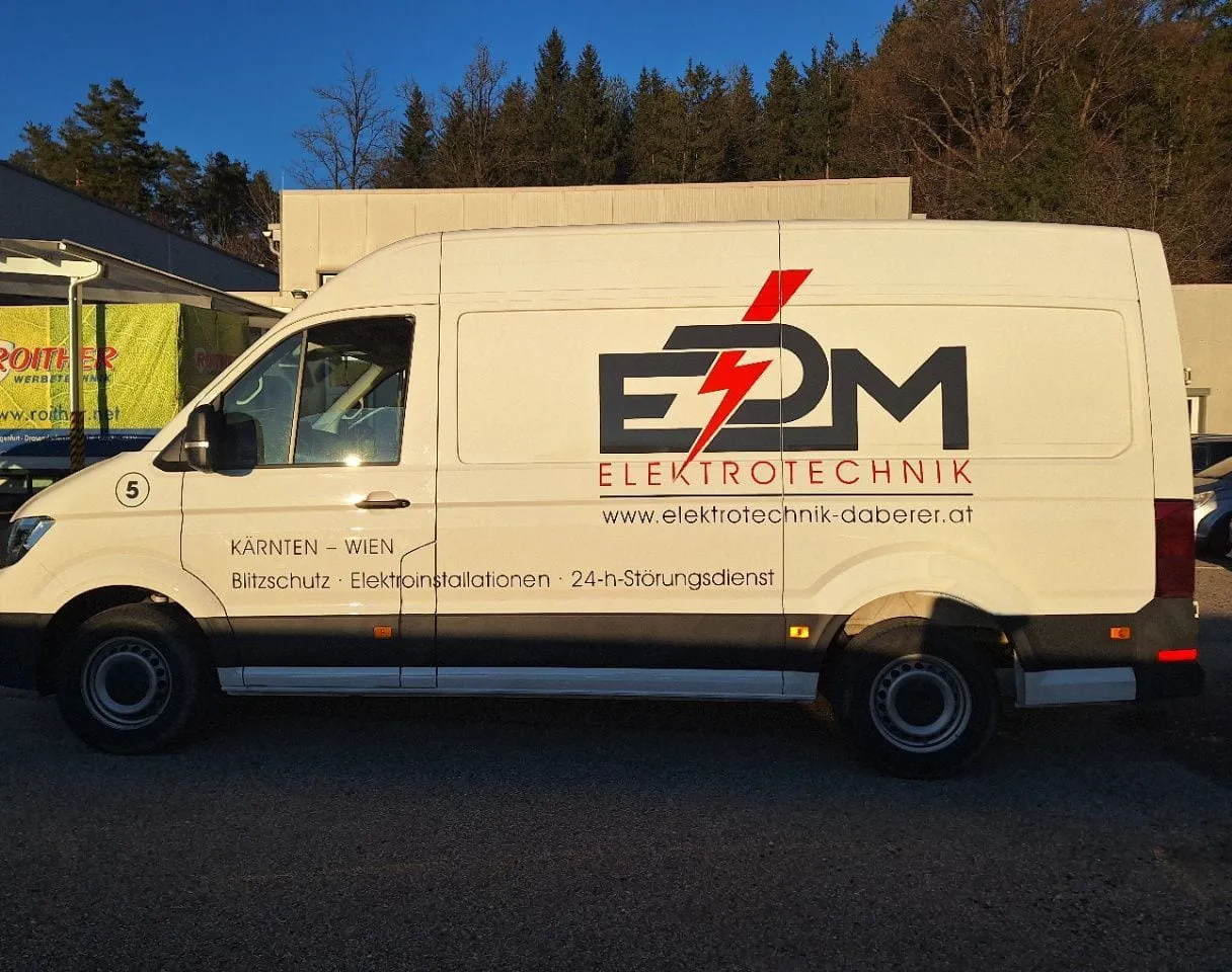 Hoher Transporter eines Elektrotechnikers mit rot-schwarzem Logo, Seitenansicht im Abendlicht vor unserem Betrieb