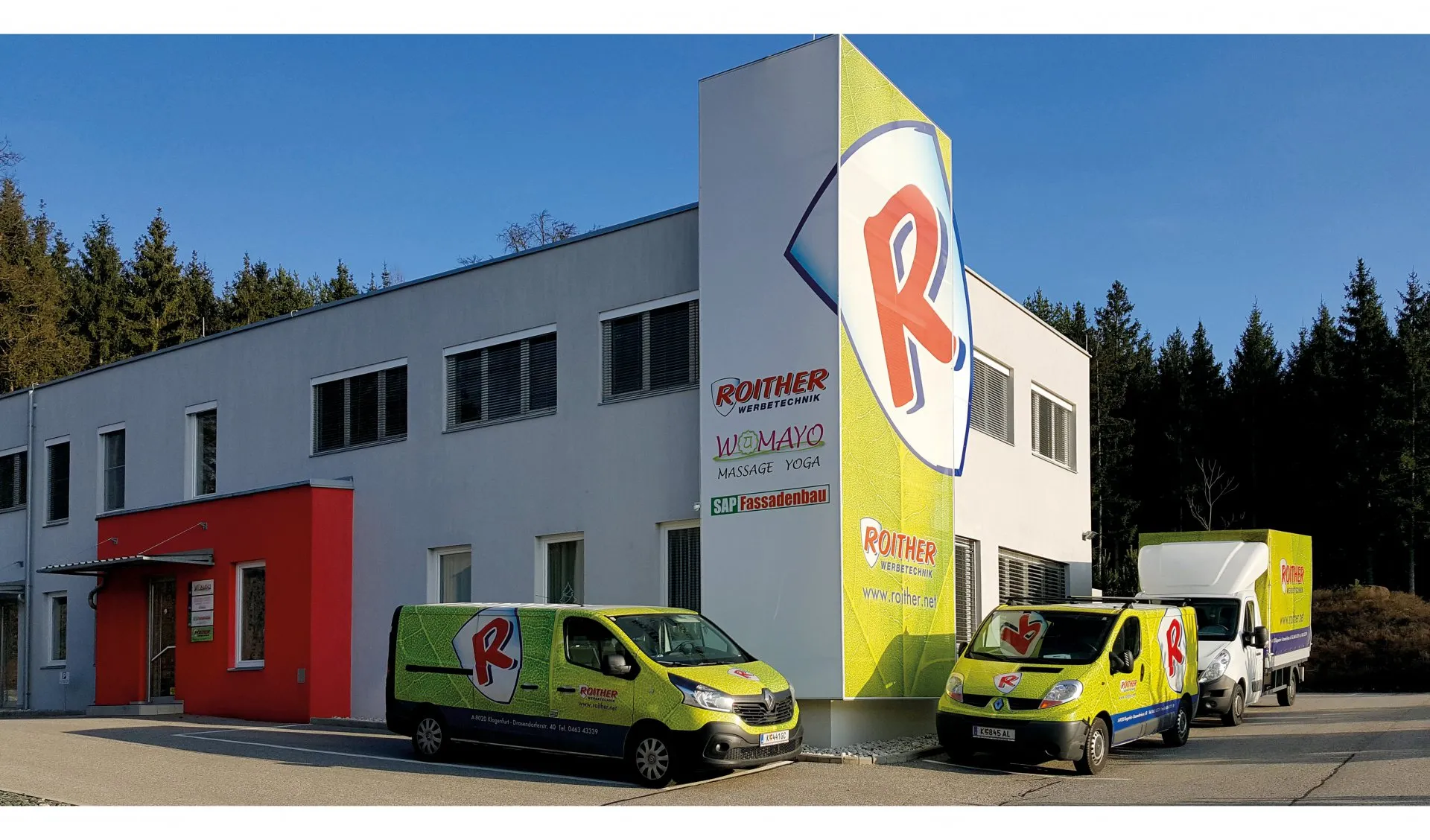 Firmengebäude von Roither Werbetechnik mit den Firmenfahrzeugen im grünen Blatt-Design